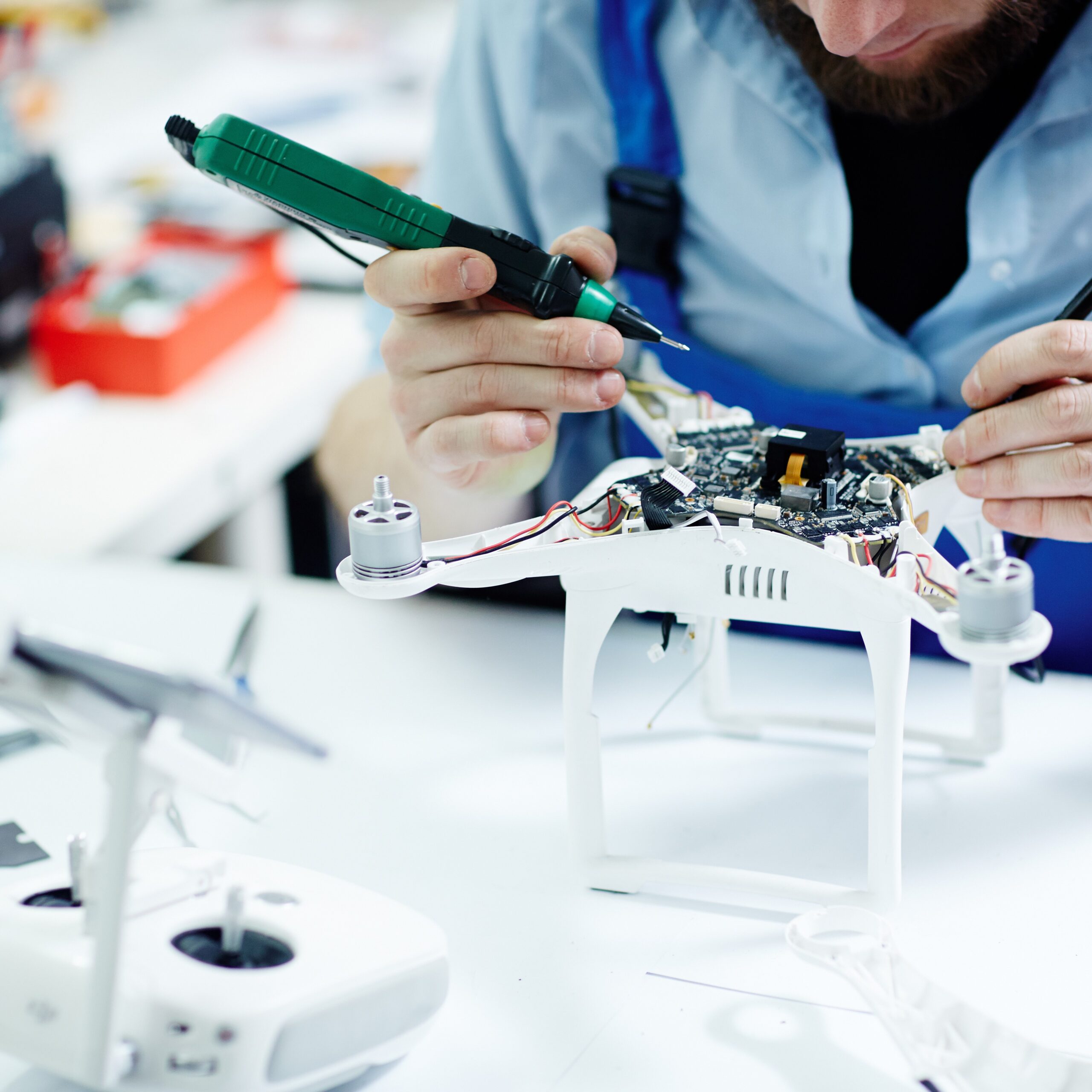 Closeup shot of unrecognizable man  testing electric current in circuit board of disassembled drone using multimeter tool on table in maintenance shop